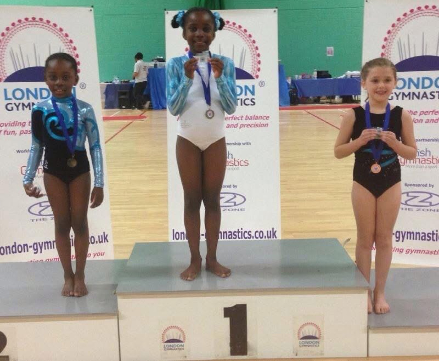 A young Rosae on the first-place podium with her medal at a London Gymnastics competition