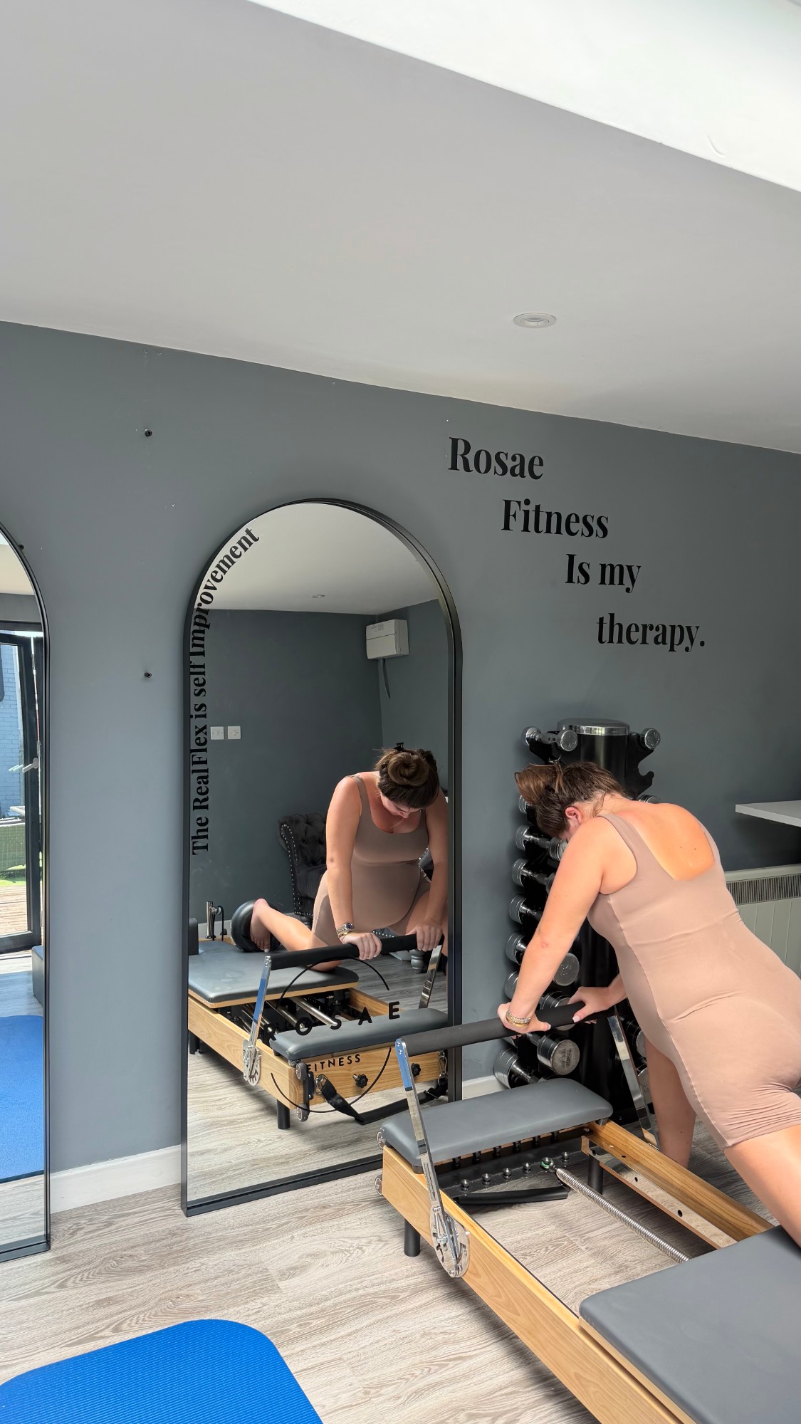 A woman coaching a reformer session in the Rosae studio, beneath the 'Rosae Fitness is my therapy' wall lettering